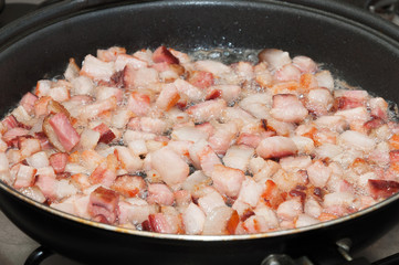 Frying bacon pieces in a pan with hot oil. Preparing ingredients to make a dish. Bacon starting to fry.