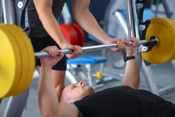 Fototapeta premium Young man lifting the barbell in gym with instructor