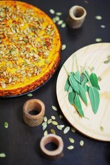 Air pumpkin pie, sprinkled with seeds on a black table next to a wooden Board sage leaves, top view closeup.