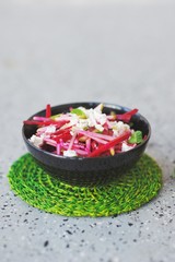 Easy diet salad with raw beets, pears, mint leaves and cheese at the black ceramic dish on a green wicker stand, closeup. Vertical layout with place for text.