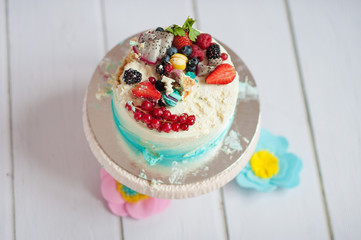 Smash cake with cream and berries on a white wooden table.