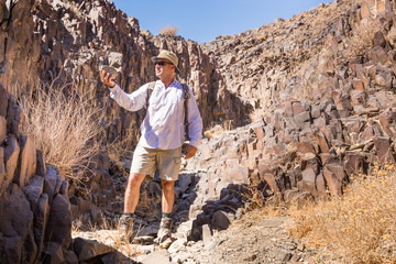 Man exploring holding rock basalt desert canyon hike.