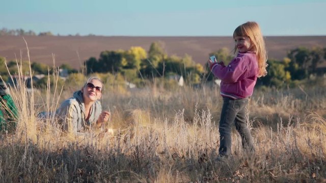 Little daughter makes photo picture of mother mom in autumn outdoor using smartphone. Slowmotion