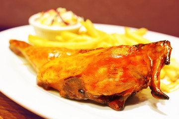 BBQ chicken quarters served with fries and coleslaw salad on white plate.