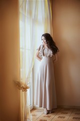 Fototapeta premium Beautiful woman in the beige dress in the bedroom