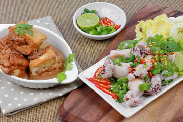Gold bar soup as fried tofu wrap minced pork in soup served with spicy and sour mixed herb salad with squid wrap minced pork on brown.  Selective focus.