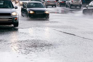 cars driving on road with water puddles during heavy rain with water splashing from the wheels