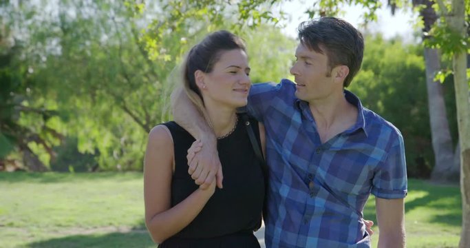 Attractive young couple sit on a table, holding each other, laughing and talking then leave while on a date in Los Angeles park.  Recorded hand-held in real time.