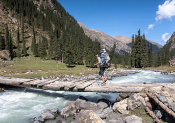 Hiker crossing river at mountains.
