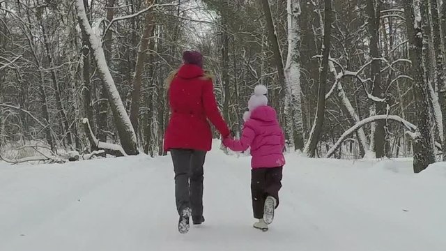 Mother with her child hold hands and run in park at winter day. Slowmotion
