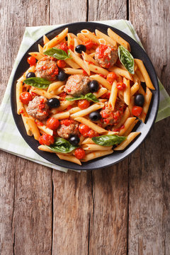 Tasty penne with meatballs, olives and tomato sauce closeup. Vertical top view