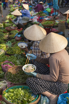 Vietnamese woman with typical conical hat , eating noodles in a street market
