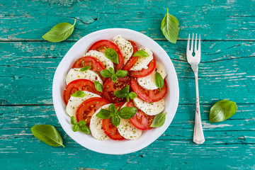 Delicious caprese salad with ripe tomatoes and mozzarella cheese with fresh basil leaves. Italian...