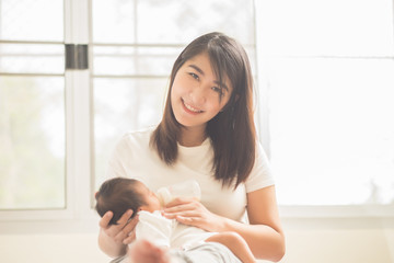 Obraz na płótnie Canvas beautiful asian mother feeding baby boy with a milk bottle at ho