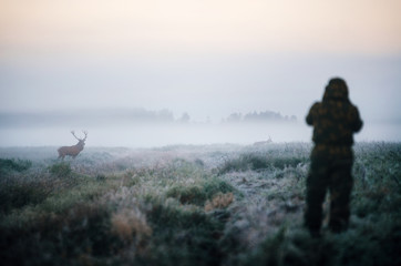 Hunter holding a rifle and aiming red deer prey in the mist, hunter photoshooting at the morning.