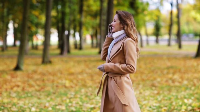 woman with smartphone walking in autumn park