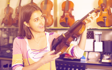 Girl choosing violin in music shop.