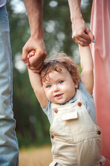 Young beautiful father, mother and little toddler son against green trees