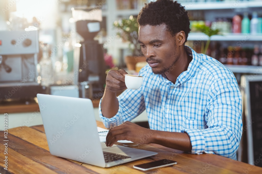 Poster man using a laptop while having cup of coffee