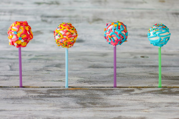 Four cake pops. Bright candies on wooden background. Go eat some sweets. Choice of taste.