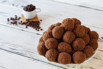 Brown sweets on a plate. Candies on white wooden background. Pile of chocolate rum balls. Cookies and cocoa powder.
