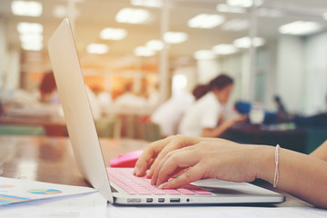 business, education, people and technology concept - close up of female hands typing on keyboard of laptop computer with Blurred education people.