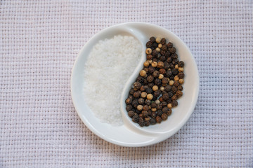 White 

linen background. is a ceramic Cup on the table. in a Cup of sea salt and pepper mixture. White 
and black pepper in a saucer. Yin and Yang