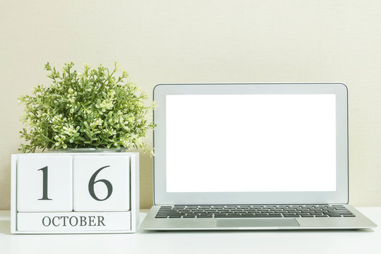 White wooden calendar with black 16 october word with white blank space at center of computer notebook on white wood desk and cream wallpaper textured background , view more date in my portfolio
