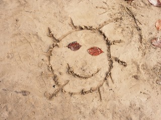 Children drawing of sun in sand on beach of bay. Eyes created from beech leaves.