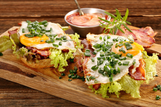 Sandwich with fried bacon, egg and vegetables on wooden backgrou