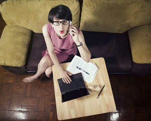 Very busy business woman emotionally talking by smartphone. On the table  next to her,  laptop , documents, glass of water.