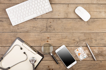 Workplace of a doctor. Stethoscope, clipboard, pills, smartphone and other stuff on wooden desk