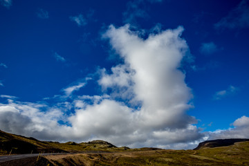 Huge white clouds in the blue sky, over a black road in West Iceland