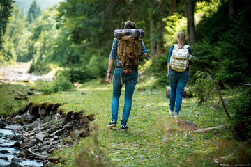 Man and woman tourists walking hand in hand through the woods in the mountains by the river