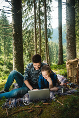 A guy and a girl tourists rest in the forest and looking in laptop