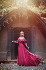 Beautiful woman in vintage burgundy dress with flying train on a background of a Gothic arch.