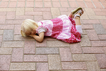 Little blond girl in pink dress lies on park path
