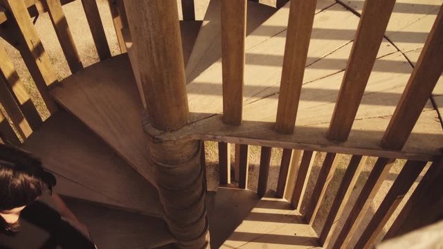 Unrecognizable brunette girl goes down on wooden spiral stairs