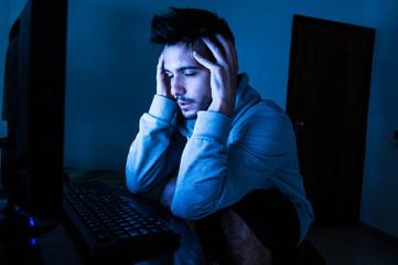 Stressed man with head in hands near computer.