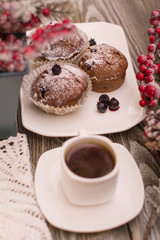 cupcake with berries on a white plate, small white cup of coffee, snowy fir branch on wooden background