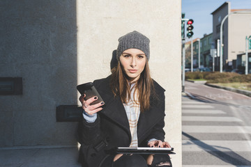 Young beautiful caucasian blonde hair woman sitting outdoor using smart phone and tablet -...