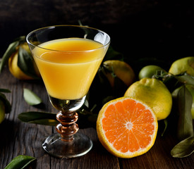 Glass of fresh tangerine juice with ripe tangerines, leaves and old-fashioned straw on a wooden background