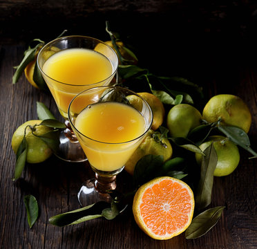 Two Glasses  of fresh tangerine juice with ripe tangerines, leaves and old-fashioned straw on a wooden background
