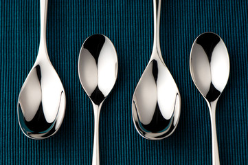 Four shining table and tea spoons in line on an elegant blue teal holiday table easily isolated for...