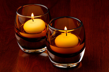 Two golden holiday candles floating in coffee colored glass holders on dark rich cherry wood table