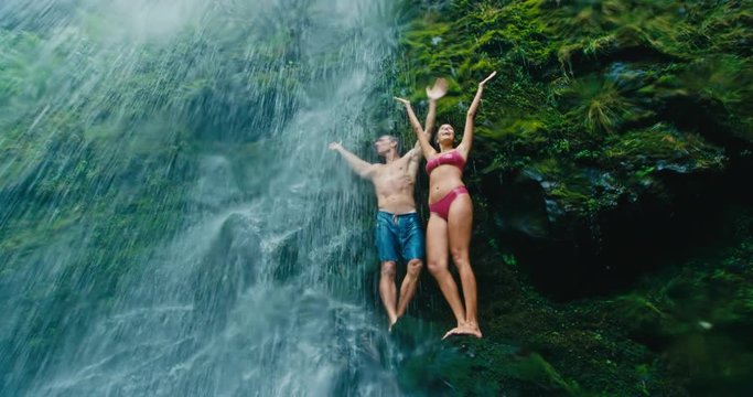 Attractive adventurous young couple relaxing under beautiful waterfall