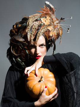 pretty woman in feather hat holds halloween pumpkin