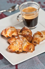 Crescents with pecan and coconut on a white square plate with a clear glass of espresso, along with a spoon and colored table cloth