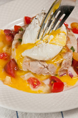 Tuna with poached egg and cherry tomatoes in a white bowl and a silver fork piercing the yoke and enveloping the tomatoes