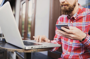 Young man texting on his smartphone and using laptop computer on an urban background